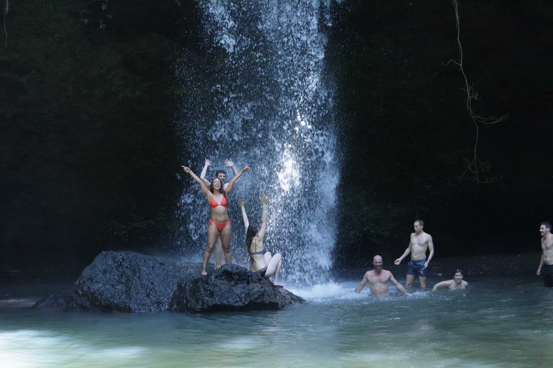 Friends laughing together beneath a waterfall in West Bali